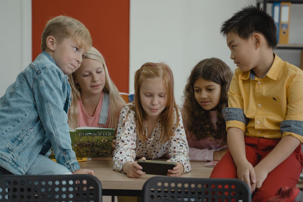 Children in a classroom using a smartphone for educational purposes, showcasing diversity and teamwork.