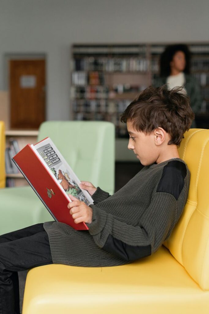 Boy engrossed in reading a book while sitting in a library, creating a tranquil educational atmosphere.